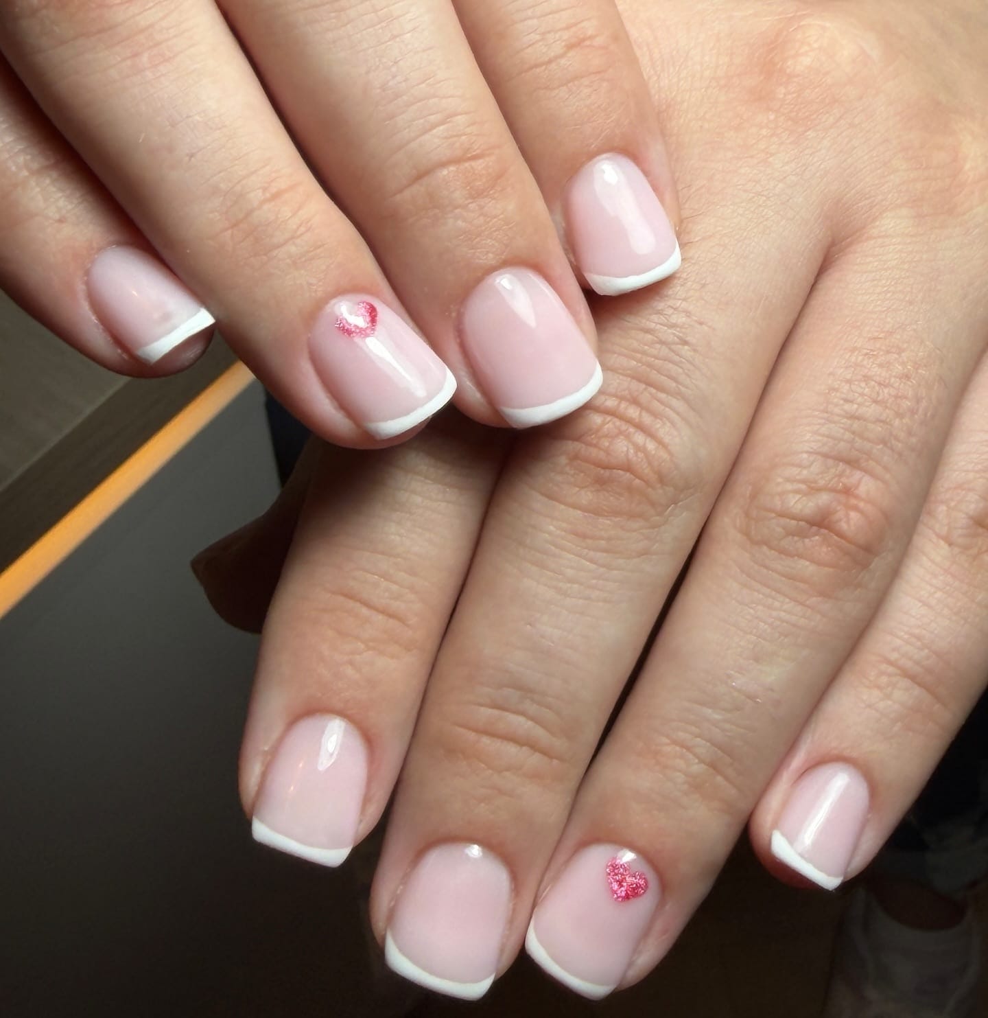 Short French gel manicure with white tips and pink glitter heart accents